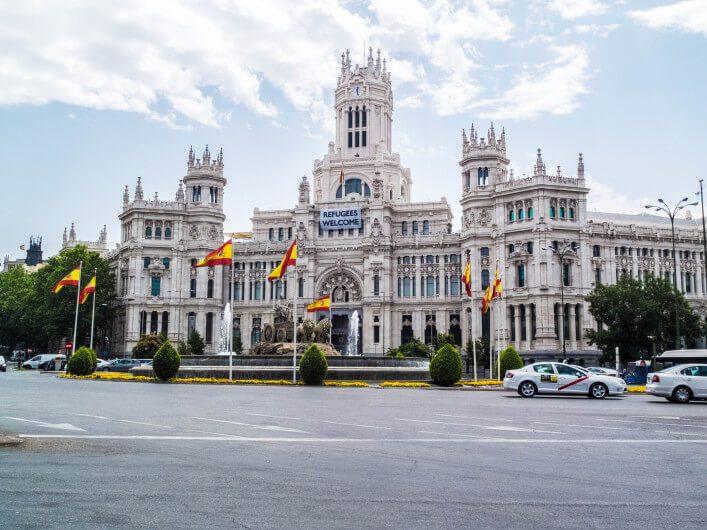 Historisches, weißes Gebäude mit reich verzierter Fassade und Türmen, zentral ein großes Banner