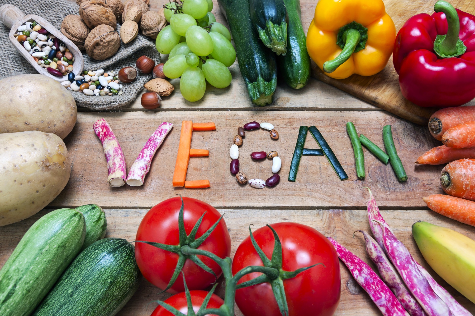 Auf einem Holztisch steht vegan mit Gemüse geschrieben.
