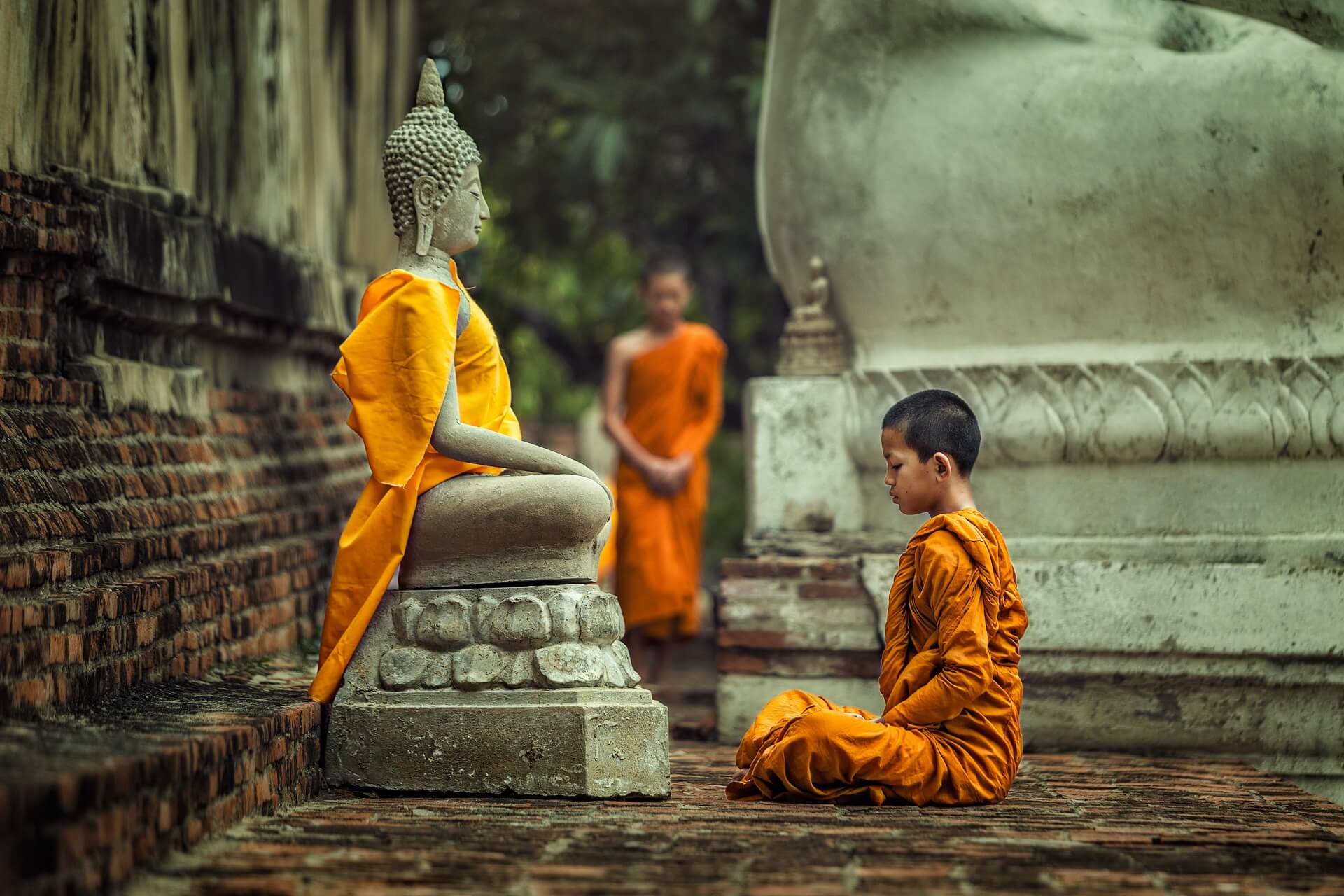 Ein kleiner Junge betet vor einer Buddhastatue