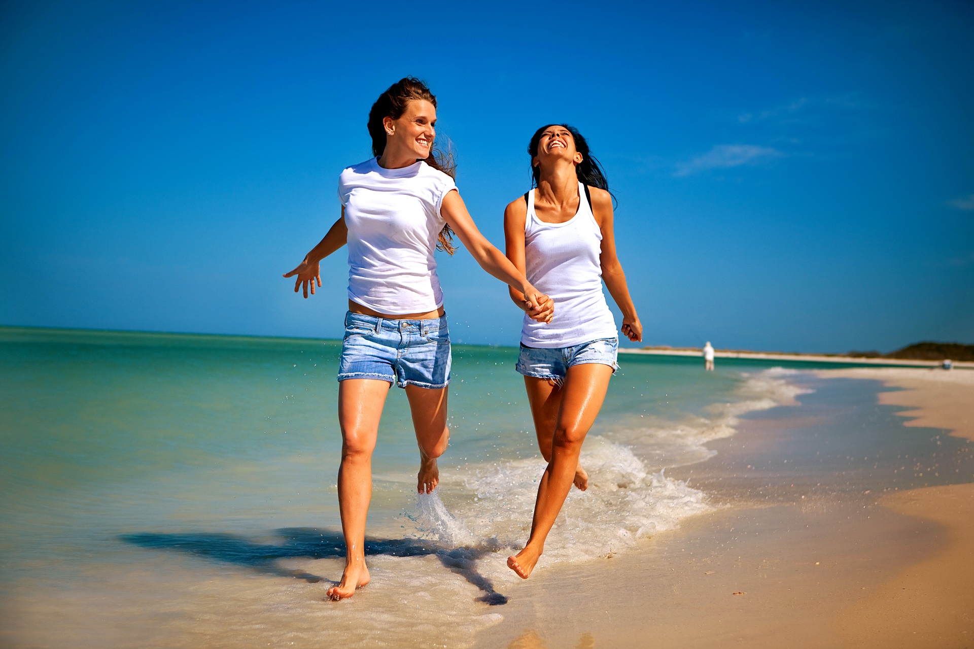 Zwei Frauen laufen Hand in Hand den Strand entlang