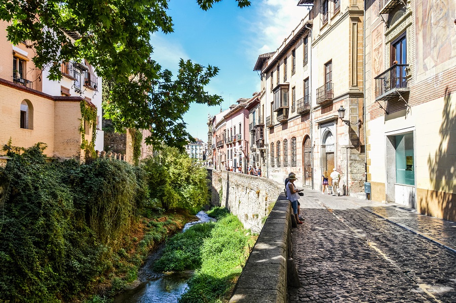 Granada, Spain - August 13, 2015: Walkway along the river in Granada, Spain. Picture taken during the day, and features tourists walking down the street and checking out the shops.