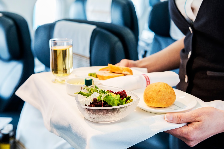 Ein Flugbegleiter serviert einem Gast an Bord eines Flugzeuges seine Mahlzeit