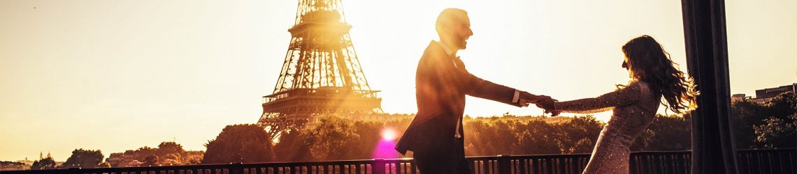 Vier Personen stehen nebeneinander und schauen mit erhobener Hand in die Ferne über das Meer. Der Himmel ist klar. Von links nach rechts: ein Mann, zwei Frauen und ein Junge. Alle lachen.