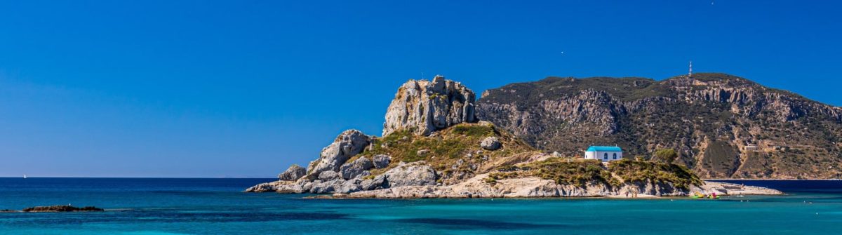 Felslandschaft mit einer kleinen Kirche vor türkisblauem Meerwasser auf der Insel Kos in Griechenland.