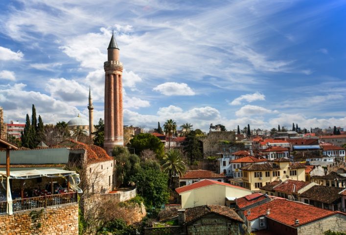Blick über die roten Dächer von Kaleici, Antalyas historischem Kern, mit einer hervorstechenden Minarettsäule vor einem blauen Himmel.