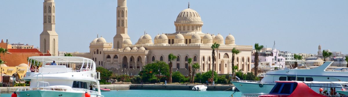 Heller Tag über dem Yachthafen Hurghadas mit der Moschee und weiß-blauen Booten im Vordergrund, klarem Himmel darüber.